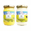 Two glass jars of Urbani Grass-Fed Himalayan ghee on a white background, one with yellow ghee (Native Cow A2) and one with white ghee (Native Buffalo). Both jars have gold lids and matching labels with a blue mountain background and yellow lower section.